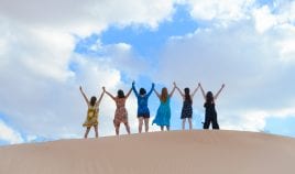 group of women in the desert, seen from behind raising their arms to the sky